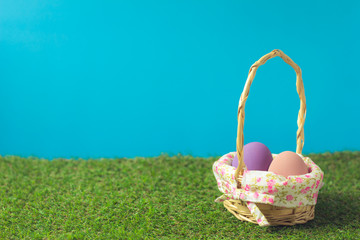 Easter eggs in a basket weave wood on the green grass.