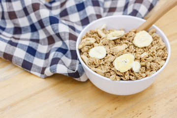 Healthy breakfast, granola with nuts and dry bananas in white blow on wooden table with wooden spoon and cute fabric.