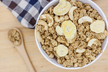Healthy breakfast, granola with nuts and dry bananas in white blow on wooden table with wooden spoon and cute fabric.