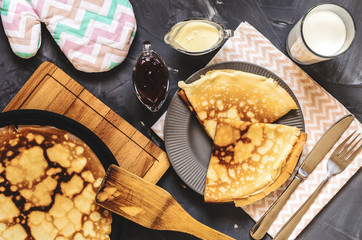 Top view of the Russian dish pancakes, milk, jam, white chocolate, towel, potholder, knife and fork.