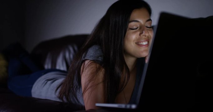4K Woman laying on the couch at night, watching TV show or a movie on her laptop