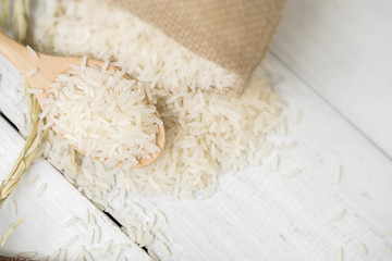 A wooden spoon filled with rice placed on wooden background.