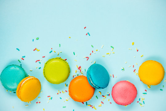 Top view of colorful macaroons and sugar sprinkles arranged over blue background.