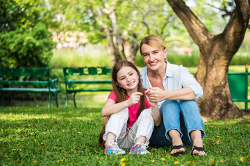 Naklejka na ściany i meble Mother and daughter relaxing sitting on grass in a park. Family and lifestyle concept