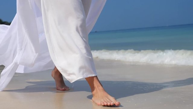 Woman Legs In White Dress Walking Barefoot Alone On The Beach On Vacation