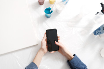 Acrylic artist's working desk top view with hands holding smart phone