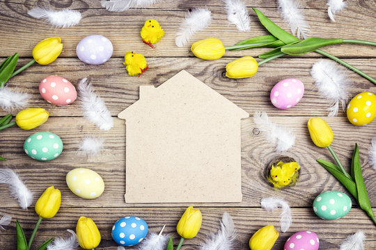 Home symbol with Easter eggs, chickens and yellow tulips on old wooden background. Space for text.