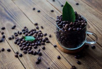 Fototapeta na wymiar cup of coffe beans and green leaf on wooden background