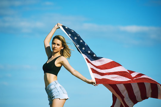 A young woman holding a us flag .The patriot girl with flag on sky background