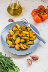 Fried potatoes in a plate. Baby potatoes, green, tomatoes and garlic on the table