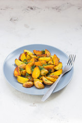 Fried potatoes in a plate. Baby potatoes, green, tomatoes and garlic on the table