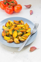 Fried potatoes in a plate. Baby potatoes, green, tomatoes and garlic on the table