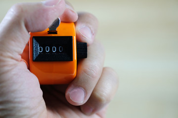 Hand holding tally counter or counting machine with 0000 number, step of coin stack on white wooden table, business and finance concept.