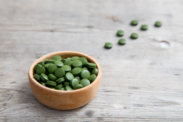 green pills spirulina or chlorella seaweed in the wooden bowl. green barley chlorella