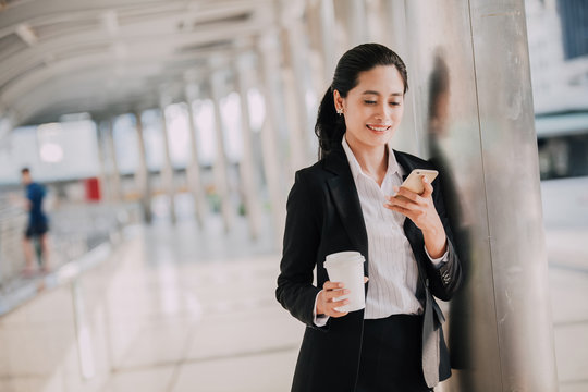 businesswoman drinking a coffee and using a digital tablet while standing in an office overlooking the city