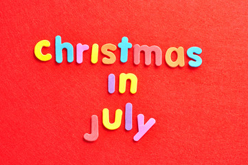 Fototapeta na wymiar The words christmas in July in colorful letters on a red background