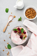 Pink raspberry banana smoothie bowl with granola, chia seeds, coconut and mint on light gray concrete background. Selective focus. Top view. Copy space.