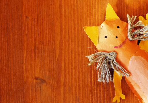 Handmade orange toy cat on red-brown wooden background as template for greeting card or postcard. Top view image with copy space for text.