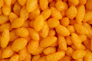 Orange spicy corn sticks closeup as background, top view.