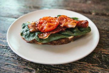 Delicious and nutritious sandwich with ham, fried tomato and greens on a plate on a wooden surface