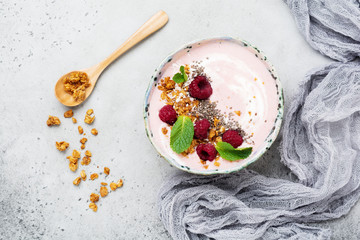 Pink raspberry banana smoothie bowl with granola, chia seeds, coconut and mint on light gray concrete background. Selective focus. Top view. Copy space.