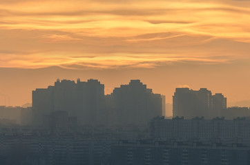 Silhouette of urban landscape with a disc of sun shining through low fibrous clouds of a polluted urban atmosphere.