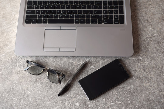 Workplace - laptop, smart phone, pen and glasses -  for working business project  on grey grunge background. Business or education concept top view image.