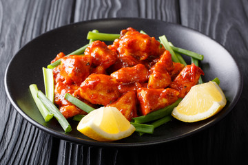 Asian food: chicken pieces in red sauce with green onions and lemon close-up on a plate.  horizontal