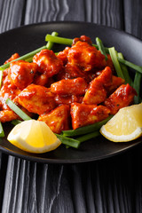 Indian chicken with spicy sauce, green onions and lemon close-up on a plate. vertical