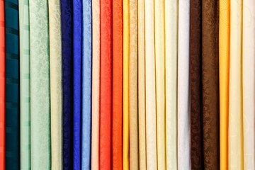 wide selection of different color textile silk fabrics clothes lay in row in drapery store