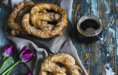 Fresh baked pretzels, tulips and coffee on shabby wooden blue background
