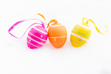 Closeup of pink, orange and yellow easter eggs with ribbons and decorated with stripes and dots laying outdoors on fresh snow in spring