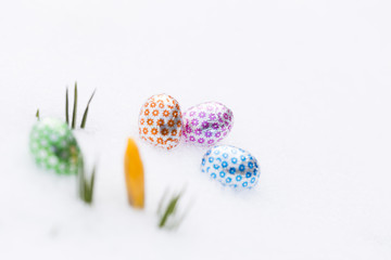 Closeup of four chocolate easter eggs wrapped in green, orange, pink and blue aluminum foil laying...