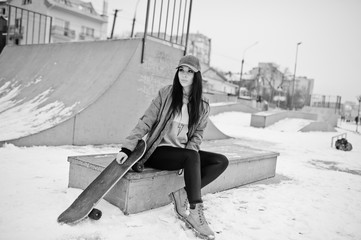 Stylish brunette girl in gray cap, casual street style with skate board on winter day.
