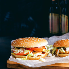 Chicken burgers and bottles of Beer. Two Homemade hamburgers on wooden tray. Black metal background.  Baking paper