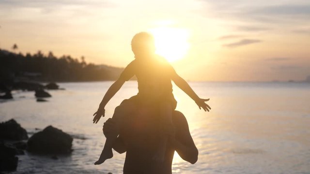 Son in eyeglasses sits on shoulders of his father raises hands imitating a flight at amazing sunset. slow motion. 3840x2160