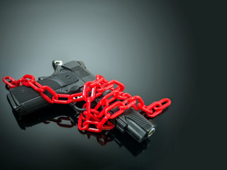 Naklejka premium reform gun control concept. red chain around handgun on black mirror with spotlight shine to the gun