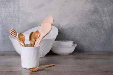 Fototapeta na wymiar A set of wooden spoons in a white bowl on a gray background on a wooden table White dishware stacked on a wooden table against grey background on wooden table