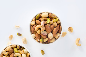 Healthy food and snack : mixed nuts in white ceramic bowl on white background from above, pistachios, almonds, hazelnuts and cashew.