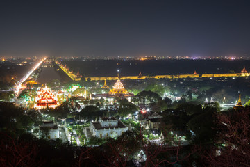 Fototapeta na wymiar Panoramic view of the lit Kyauktawgyi Pagoda, other buildings, Mandalay Palace's moat and beyond from the Mandalay Hill in Mandalay, Myanmar (Burma) at night.