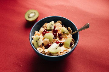 delicious crispy cornflakes with kiwi pieces and cranberries in bowl,  healthy breakfast on red background