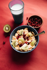 delicious crispy cornflakes with kiwi pieces and cranberries in bowl,  healthy breakfast on red background
