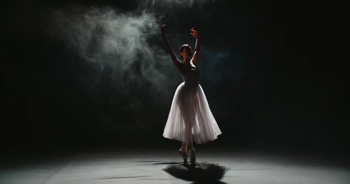 4K video footage of silhouette of beautiful female ballet dancer in white tutu on black background, slow motion