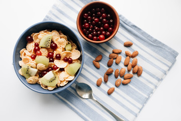 delicious crispy cornflakes with kiwi pieces and cranberries in bowl, almonds on dish cloth, closeup, healthy breakfast 