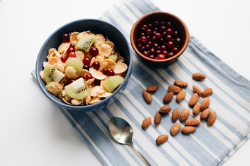 glass of milk, delicious crispy cornflakes with kiwi pieces and cranberries in bowl, almonds on dish cloth, closeup, healthy breakfast 