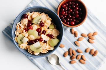 glass of milk, delicious crispy cornflakes with kiwi pieces and cranberries in bowl, almonds on dish cloth, closeup, healthy breakfast 