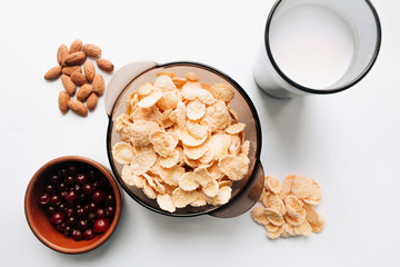 delicious crispy cornflakes in bowl with cranberries, glass of milk and almonds  on white background,  healthy breakfast