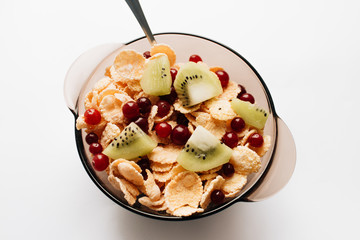 delicious crispy cornflakes with kiwi pieces and cranberries in bowl on white background, closeup,...