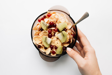 female hand holding bowl with delicious crispy cornflakes, kiwi pieces and cranberries on white background, closeup, healthy breakfast 