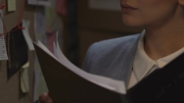 Woman detective revising folder with criminal case information, looking clues